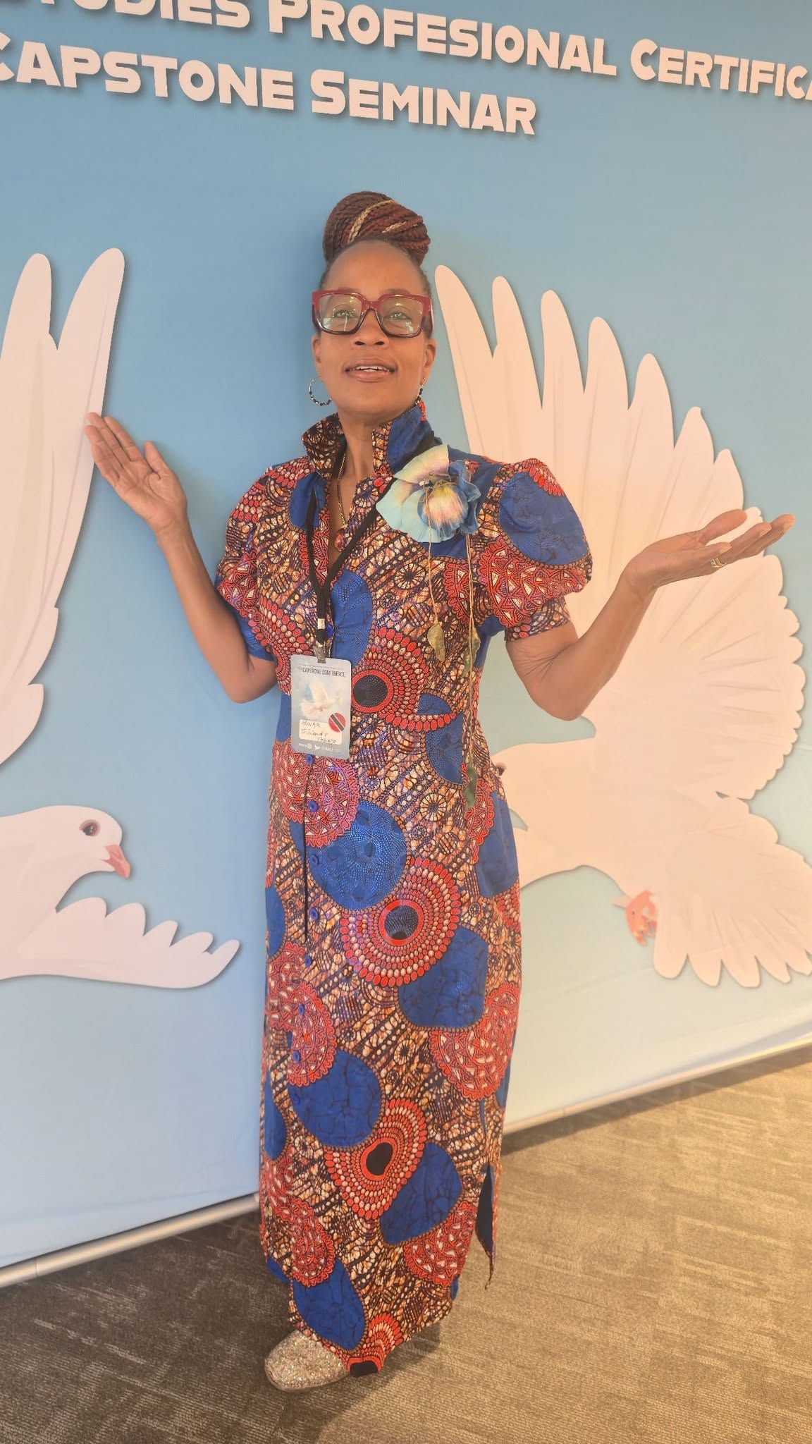 Anika in an Ankara dress at the Capstone Seminar with a peace doves backdrop