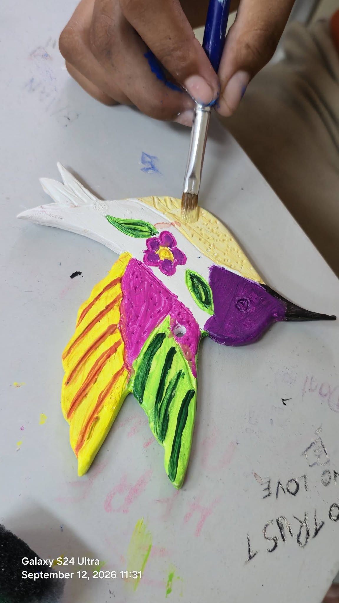A child painting a colorful clay hummingbird