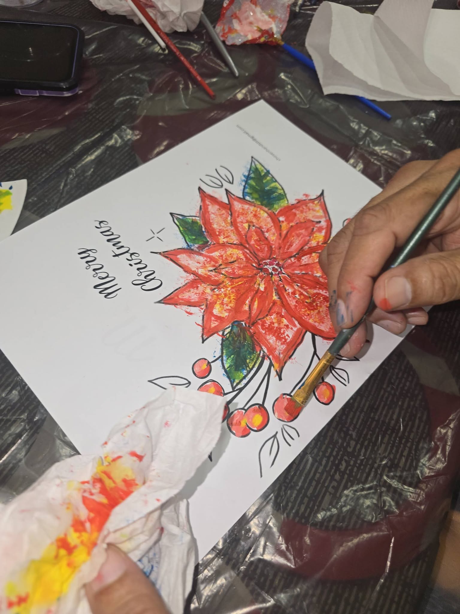 A hand painting a poinsettia on a Merry Christmas artwork